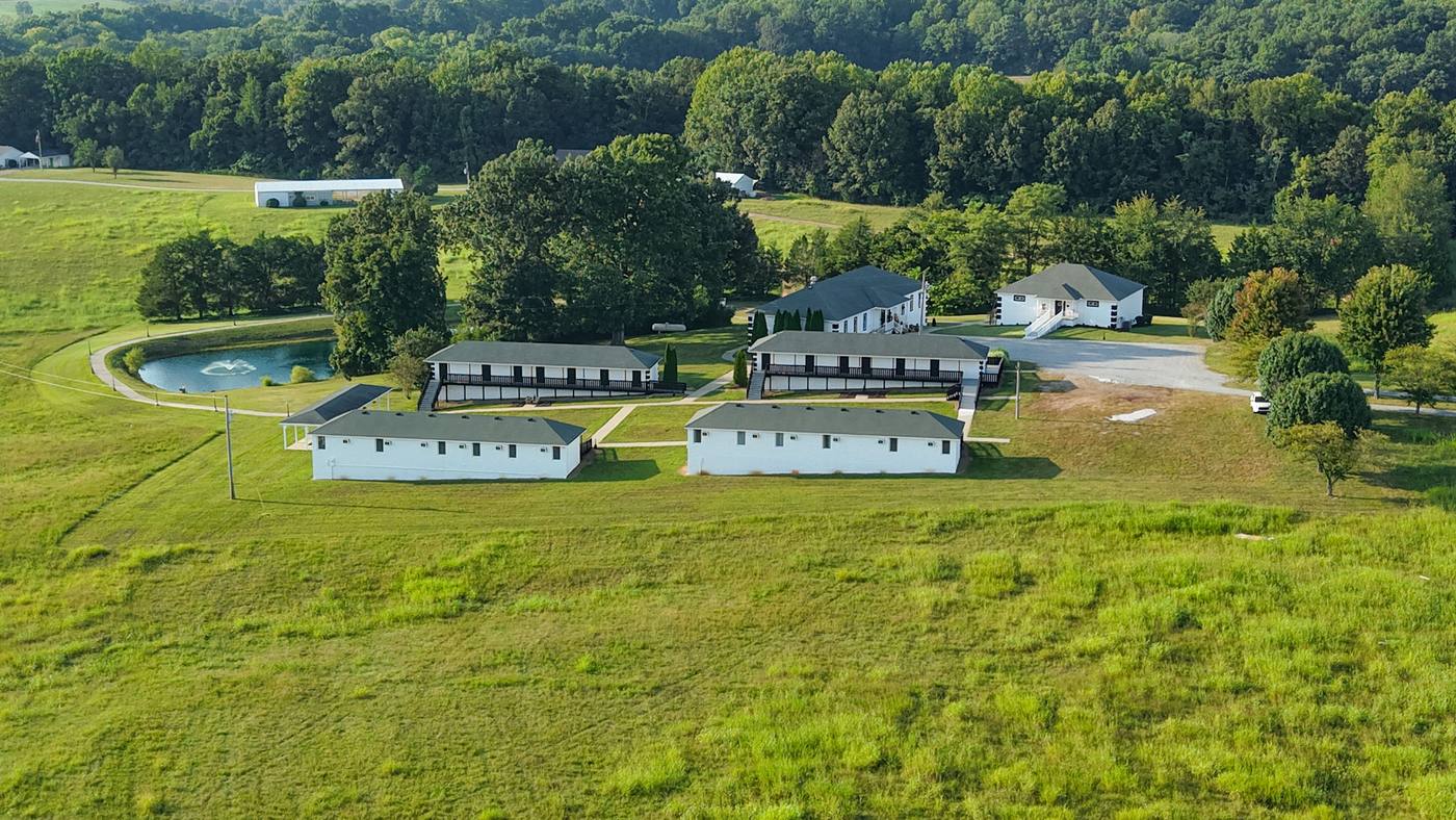 Aerial view of the whole ranch — pond, residence buildings, pavilion and gravel drive across mown fields